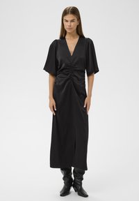 Mustmust mustrõiv must must V-kaelusega, kortsunud vöökohaga, voolavad varrukad ja ees oleva lõhega. Ühendatud põlvekõrguste, liibuvate mustade saapadega.