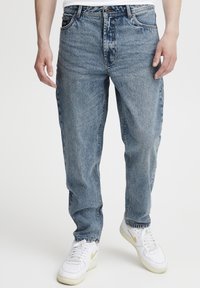 Blå denimjeans med avslappet passform, midt på livet, klassisk femlommersdesign og lett falming. Kombinert med hvite joggesko.