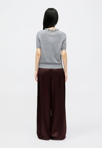 Γκρι κοντομάνικο μπλουζάκι με υφή στο λαιμό, φορεμένο με ροών παντελόνι μπορντό σε φαρδιά γραμμή. Η οπίσθια όψη αποκαλύπτει λεπτομέρεια με κλειδαρότρυπα στον λαιμό.