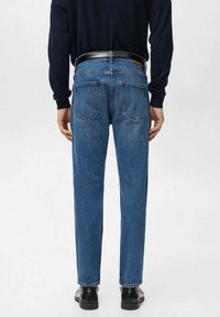 Vaqueros ajustados de mezclilla azul con cinco bolsillos, detalles cosidos y un cinturón de cuero negro, combinados con un suéter oscuro y zapatos negros.