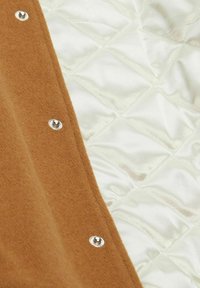 Tessuto trapuntato con una finitura lucida di colore verde pallido, completato da un pannello in lana marrone e bottoni automatici metallici lungo il bordo.