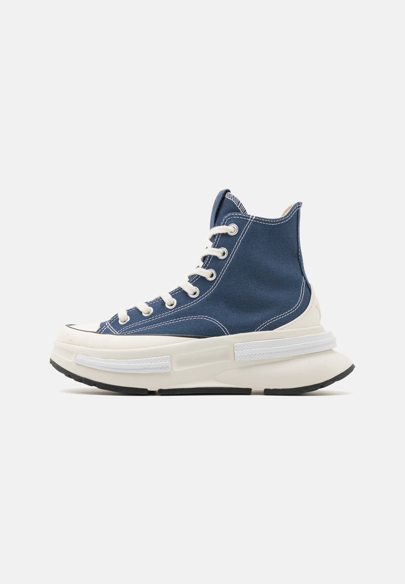 Blue canvas high-top sneakers with beige rubber sole. Features white laces, contrasting stitching, and a chunky sole design.