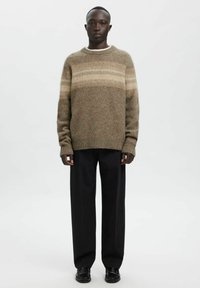 Pull en laine marron avec des rayures horizontales claires, poignets côtelés et encolure ronde, associé à un pantalon large noir et des chaussures noires.