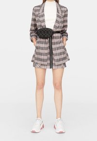 Abito blazer a quadri in rosa e grigio, doppiopetto con vita regolabile, abbinato a sneaker bianche. Presenta tasche e una finitura foderata.