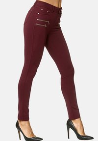 Pantaloni skinny bordeaux con dettagli in zip argentati sulle tasche anteriori e una texture liscia. Abbinati a scarpe con tacco nere.