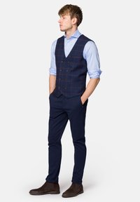 Granatowy kamizelka w kratę na jasnoniebieskiej koszuli, w połączeniu z ciemnymi spodniami i brązowymi butami chelsea. Charakteryzuje się dopasowanym krojem i pięcioma guzikami.