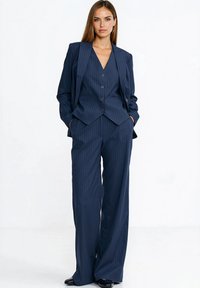 Garnitur w granatową prążkowaną tkaninę, składający się z dopasowanej marynarki z kołnierzem i zapięciem na guziki, w zestawie z szerokimi spodniami i ozdobnymi kieszeniami.