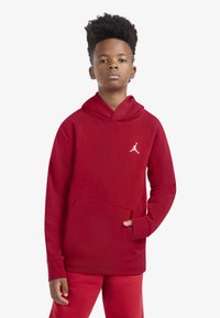 Rdeča bombažna jopa s sprednjim žepom in kapuco z vrvico. Na prsih je bel logotip Jumpman. Kombinirano z ujemajočimi rdečimi hlačami.