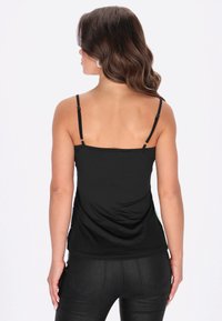 Fekete, vékony, állítható pántokkal ellátott top, testhez simuló kialakítással, puha anyagból és sima textúrával, fekete nadrággal párosítva.