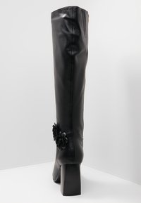 Czarny skórzany kozak za kolano na słupku. Z boku ozdobiony kwiatowym akcentem. Gładka tekstura, dopasowany fason.