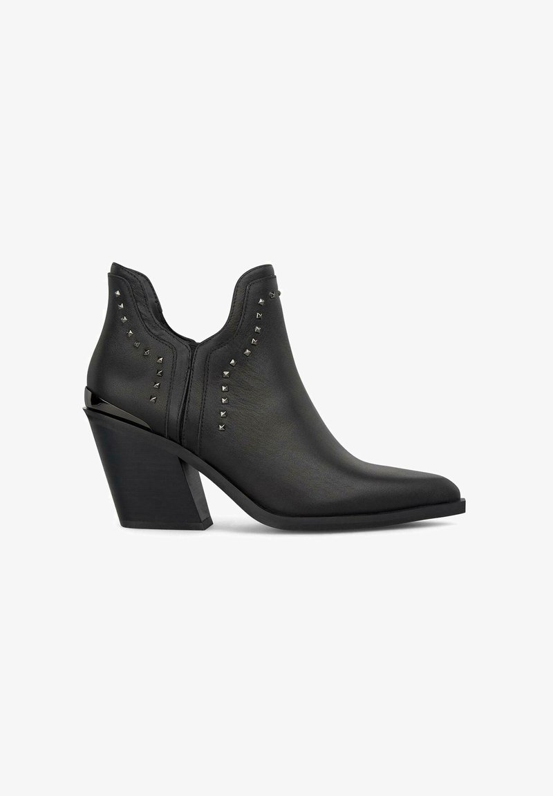 Botín negro de cuero hasta el tobillo, con punta afilada, tacón angular y adornos con tachuelas a lo largo de los lados. Textura suave y diseño minimalista.