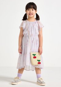 Robe florale violette clair avec des manches volantées, associée à un sac en osier avec des cerises rouges. Des baskets argentées et des chaussettes pastel complètent le look.