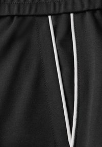 Pantalon en tissu noir avec une ceinture élastique et deux cordons blancs verticaux suspendus au centre avant.