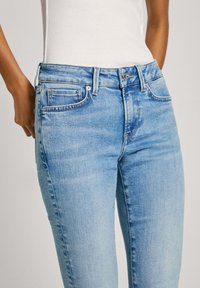 Ljusblå denimjeans med klassisk passform, subtil blekning, fem fickor och midjebandknäppning; tyget ser slätt och något texturerat ut.
