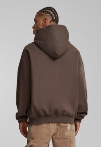 Sudadera con capucha en color marrón, de corte relajado, con puños y bajo acanalados. Presenta una textura suave y una capucha sobredimensionada, vista desde la parte de atrás.