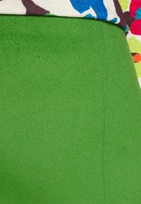Tessuto verde, morbido con una superficie liscia, caratterizzato da una cucitura verticale. Un materiale colorato e a fantasia è visibile nella parte superiore.