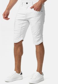 Shorts en jean blanc avec une coupe ajustée, poches latérales et revers roulés, associés à des baskets blanches avec un accent noir au talon.