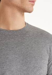 Šedé crewneck tričko vyrobené z měkké bavlněné látky; má krátké rukávy a hladký povrch. Bez vzorů nebo ozdob.