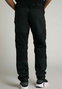 Zwarte cargobroek met een elastische tailleband, taps toelopende boorden en verschillende structuren. Voorzien van ritszakken en versterkte kniestukken.