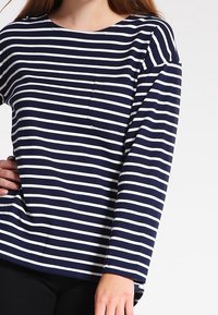 Navy och vita randiga långärmade skjorta med rund halsringning och en liten bröstficka. Tillverkad av mjukt material och har en avslappnad passform.