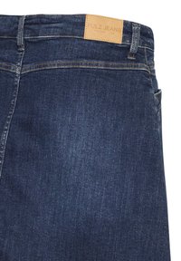Tumši zili džinsi no denima ar redzamiem šuvēm un smilšu krāsas ādas etiķeti ar uzrakstu "PULZ JEANS" jostasvietā.