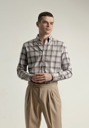 Camisa de cuadros en tonos grises claros y marrones, hecha de tela con cuello abotonado. Los pantalones son beige con pliegues y detalle de botón.