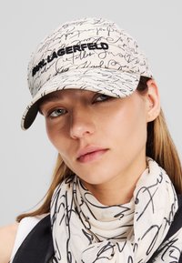 Weißes Cap mit schwarzem handgeschriebenem Aufdruck, der "Karl Lagerfeld" in Schwarz gestickt zeigt. Glattes Material mit gebogenem Schirm.