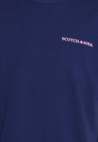 Námořnická modrá bavlněná trička s kulatým výstřihem a růžovým vyšívaným logem "SCOTCH & SODA" na levém horním rohu.