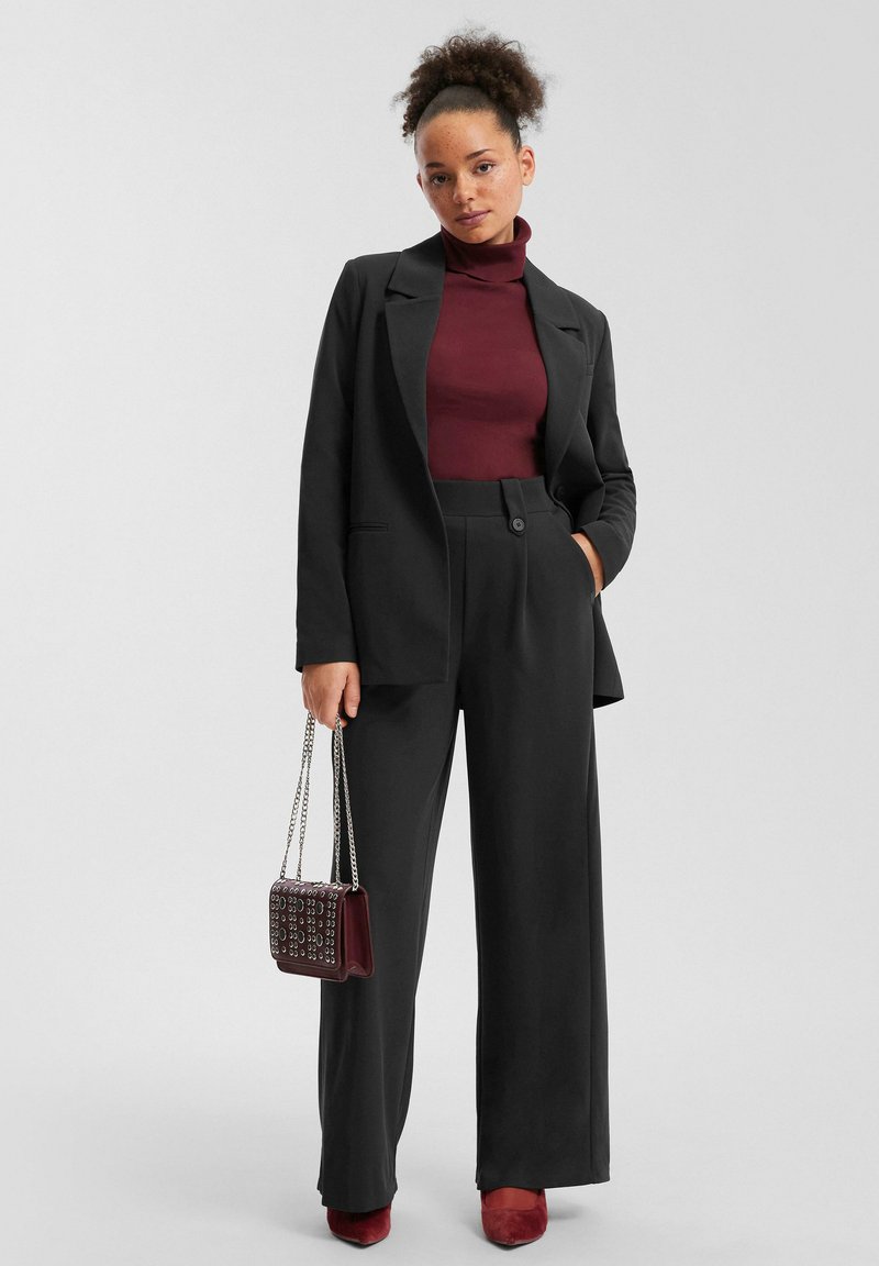 Must mustriga mustriga ja laia jalaga püksid, mida on kombineeritud burgundia värvi turtlenecki ja sobivate sametist kingadega. Väike, nupuga käekott.