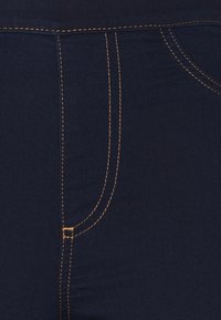 Tela de color azul oscuro con una textura suave, realzada por costura naranja en contraste a lo largo de las costuras y los bordes de los bolsillos.