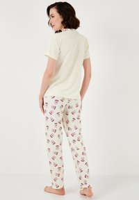 Haut à manches courtes rayé jaune clair et pantalon de pyjama crème avec un imprimé de boissons rouges et de lèvres. Matière en coton douce, coupe décontractée.