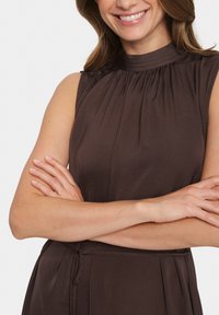 Rochie maro fără mâneci, cu guler înalt, dintr-un material pliat și accent la talie cu un nod. Textură netedă cu o strălucire subtilă.