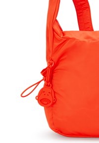 Borsa in nylon arancione con una texture liscia, caratterizzata da un distintivo portachiavi a forma di faccia di scimmia come accento. Forma strutturata con manici robusti.