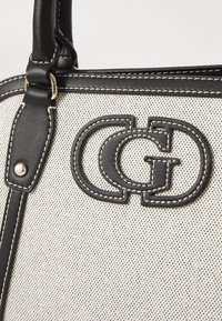 Borsa in bianco e nero con superficie testurizzata, caratterizzata da un logo prominente e cuciture a contrasto; arricchita da dettagli in pelle e metalli.