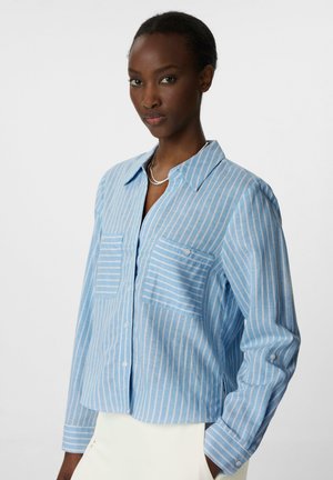 Light blue button-up shirt with white vertical stripes, two front pockets, and long sleeves featuring buttoned cuffs. Soft fabric texture.