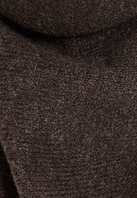 Tissu en laine marron foncé avec une texture douce et duveteuse, présentant des fibres étroitement tricotées visibles en gros plan.