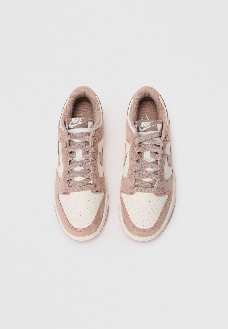Sneakers Nike rosa e beige con finitura in suede testurizzato, punta perforata e lacci piatti. Presentano un logo Swoosh bianco sul lato.