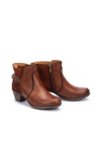 Braune Lederankelstiefel mit einem Reißverschluss, geschwungenem Design und einer dekorativen runden Hardware-Akzent. Niedriger Blockabsatz, glatte Textur.