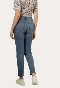 Jeans de ganga azul clara com corte slim e cintura alta, com bolsos traseiros e um ligeiro desbotado. Combinados com uma blusa estampada e ténis brancos.