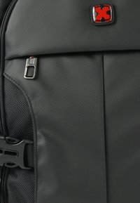 Zwarte gestructureerde rugzak met zilveren ritsbeslag en een klein rood logo. Zichtbare zijnetzak, met een verstelbare riemgesp.