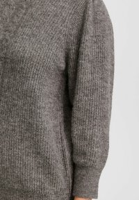 Pull en tricot gris avec une surface texturée, présentant une coupe ample et des manches trois-quarts. Matériau chaud et doux avec un aspect confortable.