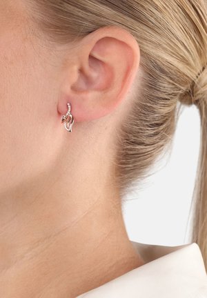 Pendientes de plata que representan una forma fluida, con una pequeña fila de piedras preciosas transparentes. El diseño tiene una estética elegante y moderna.