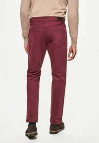 Pantalons en coton bordeaux avec une coupe slim, design à cinq poches et détails de couture subtils ; portés avec des chaussures marron foncé.