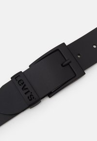 Černý kožený opasek s obdélníkovou kovovou sponou s vyraženým logem "Levi's" a několika otvory pro nastavení na pásku.