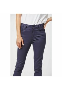 Marineblauwe stretchjeans met een slim fit, voorzien van een knoopsluiting, vijf zakken en een subtiele textuur. Draag met een wit T-shirt.