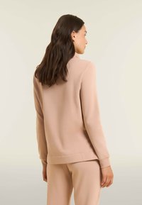 Sweatshirt rose clair à manches longues, texture douce, poignets et col côtelés. Design simple, associé à un pantalon assorti.