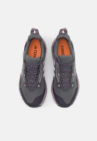 Grau-lilafarbene Wanderschuhe aus Mesh-Material, mit auffälligen Schnürsenkeln, gepolsterten Zungen und weißen Akzenten an den Seiten. Orangefarbene Innensohlen sichtbar.