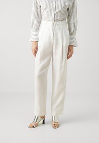 Witte linnen broek met een trekkoord in de taille, gecombineerd met een gestreept overhemd met knopen en metallic zilveren haksandalen.