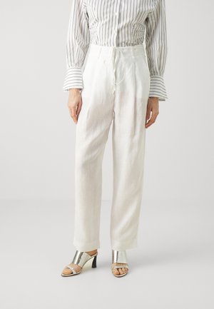 White linen trousers with a drawstring waist, paired with a striped button-up shirt and metallic silver heeled sandals.