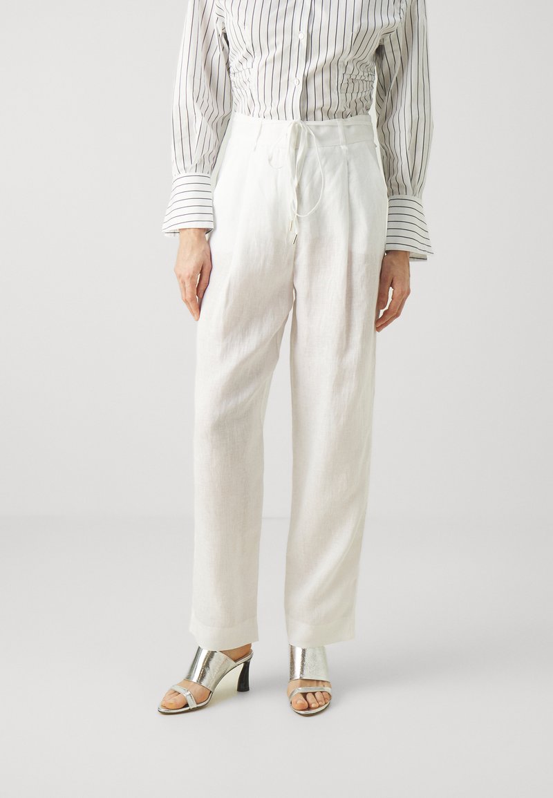Witte linnen broek met een trekkoord in de taille, gecombineerd met een gestreept overhemd met knopen en metallic zilveren haksandalen.